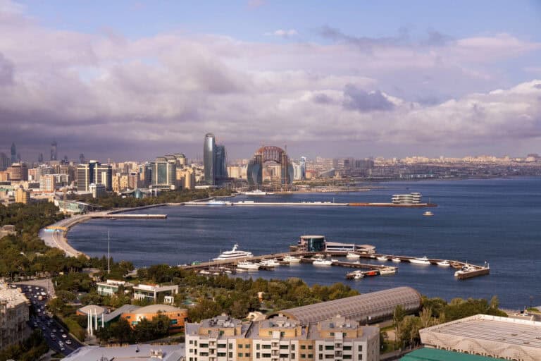 נוף עירוני של חוף ובו מבנים מודרניים, טיילת מעוקלת על קו המים, יאכטות העוגנות במרינה ושמיים מעוננים חלקית. - Kerato Life מה שלא עשה הטבע עושה הצבע